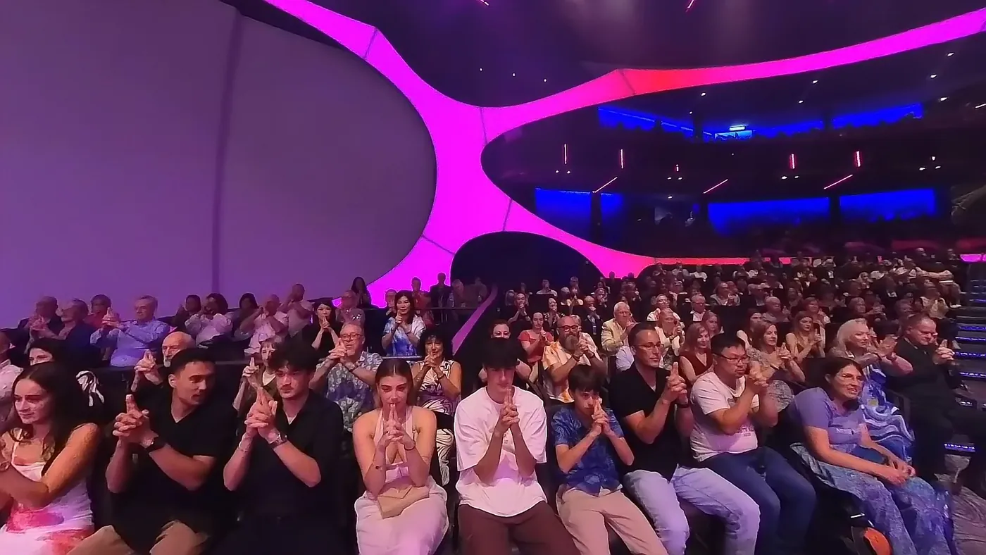A full theatre with the whole audience taking part, hands locked together during the routine